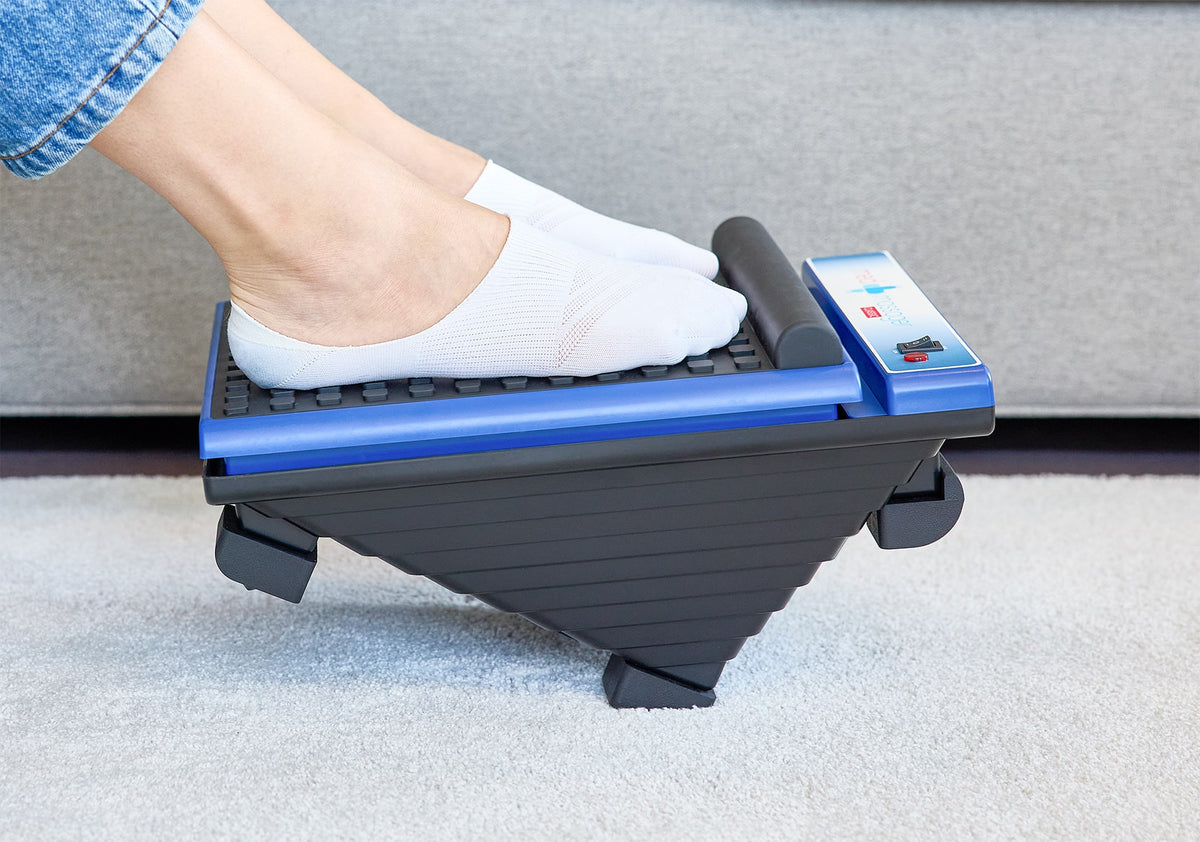 Person wearing white socks using blue and black MedMassager foot massager on carpeted floor.