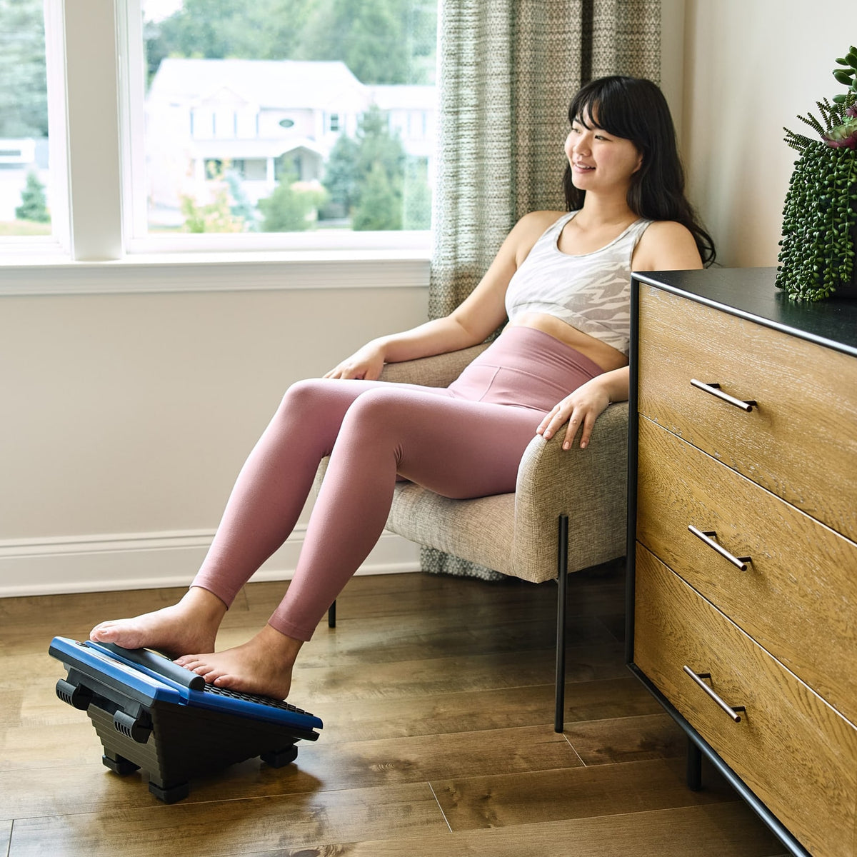 Woman relaxing in a modern room with feet on MedMassager foot massager, smiling and comfortable.