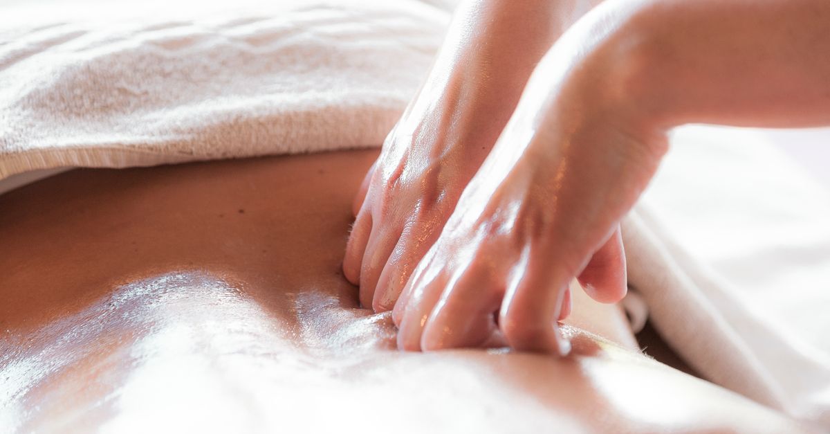 Close-up of hands giving a soothing back massage with oil in a tranquil spa setting.