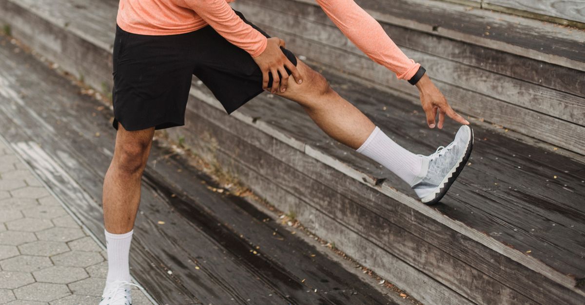 Adult man stretching leg on wooden steps in outdoor setting, promoting healthy lifestyle.