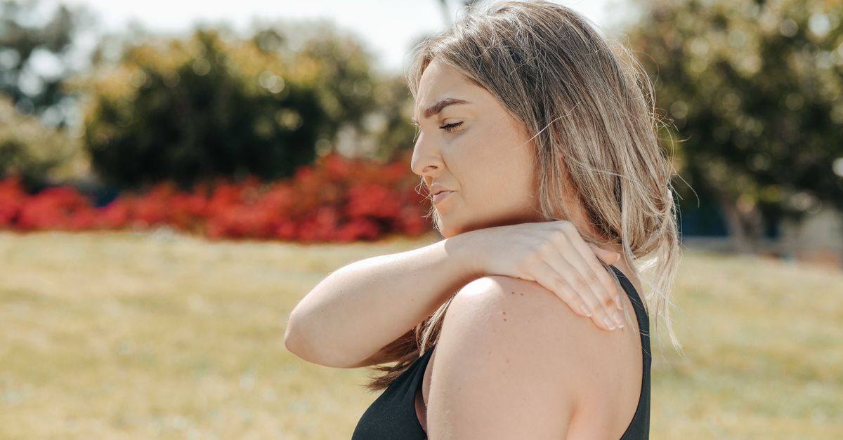 Woman in black tank top touching shoulder outdoors. Concept of shoulder pain and relaxation.