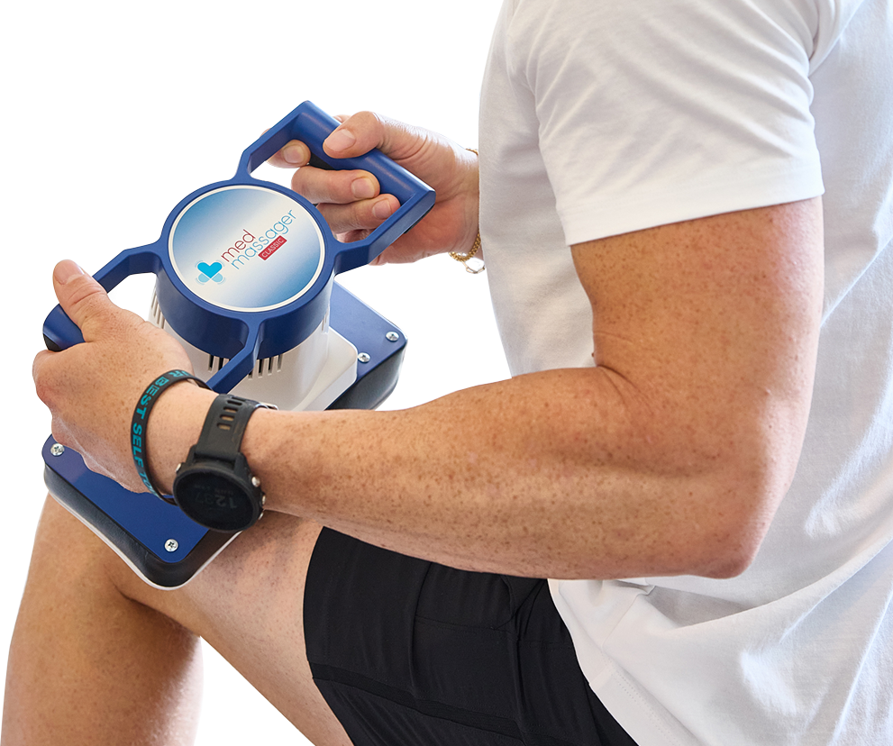 Person using a MedMassager body massager on their thigh for muscle relief, wearing a white shirt.