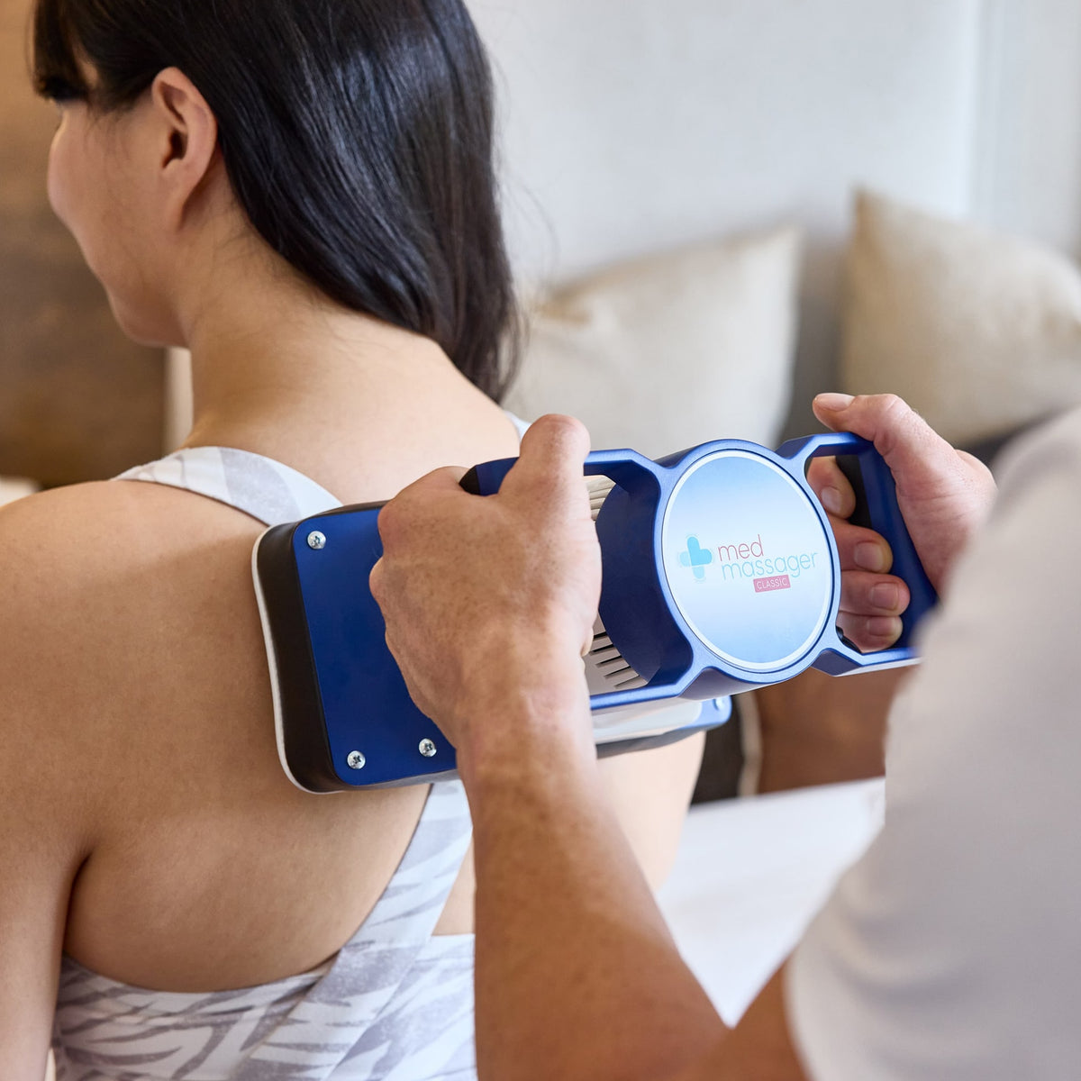Body massager being used on a woman’s upper back in a cozy home setting.