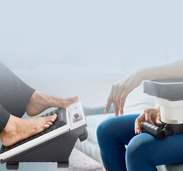 Two people on a couch using MedMassager devices, one with a foot massager and the other with a hand massager.