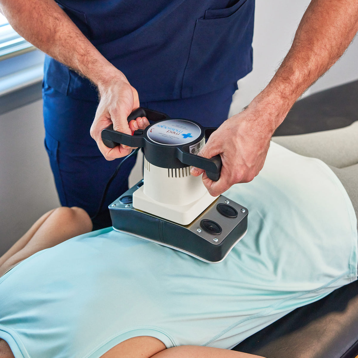 Body massager used on back for pain relief while person lies on treatment table.