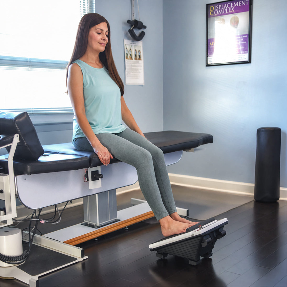 Woman using MedMassager foot massager in a clinic room to stretch her legs while seated.