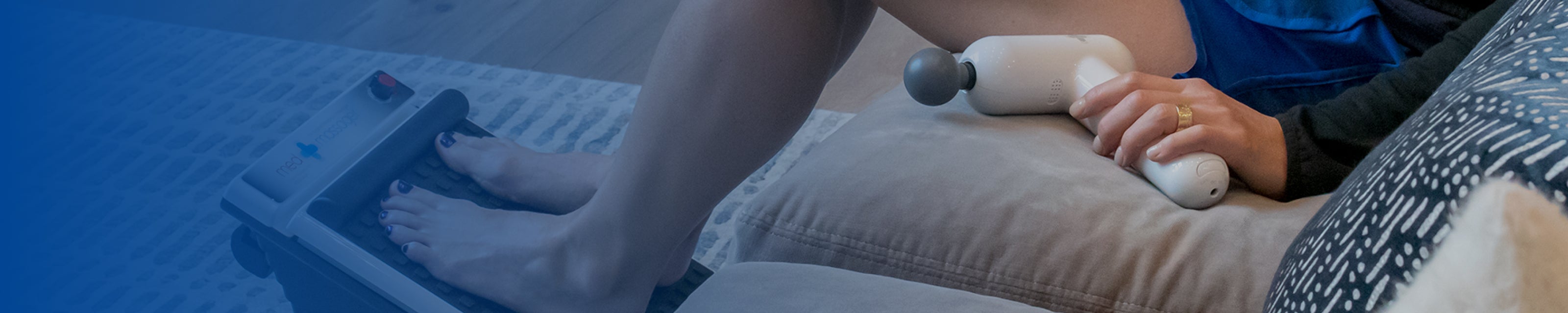 Person using a body massager on their leg while feet rest on a foot massager at home.