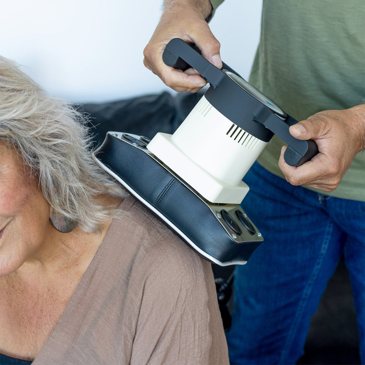 Woman uses MedMassager body massager on upper back while sitting on couch for neuropathy relief.