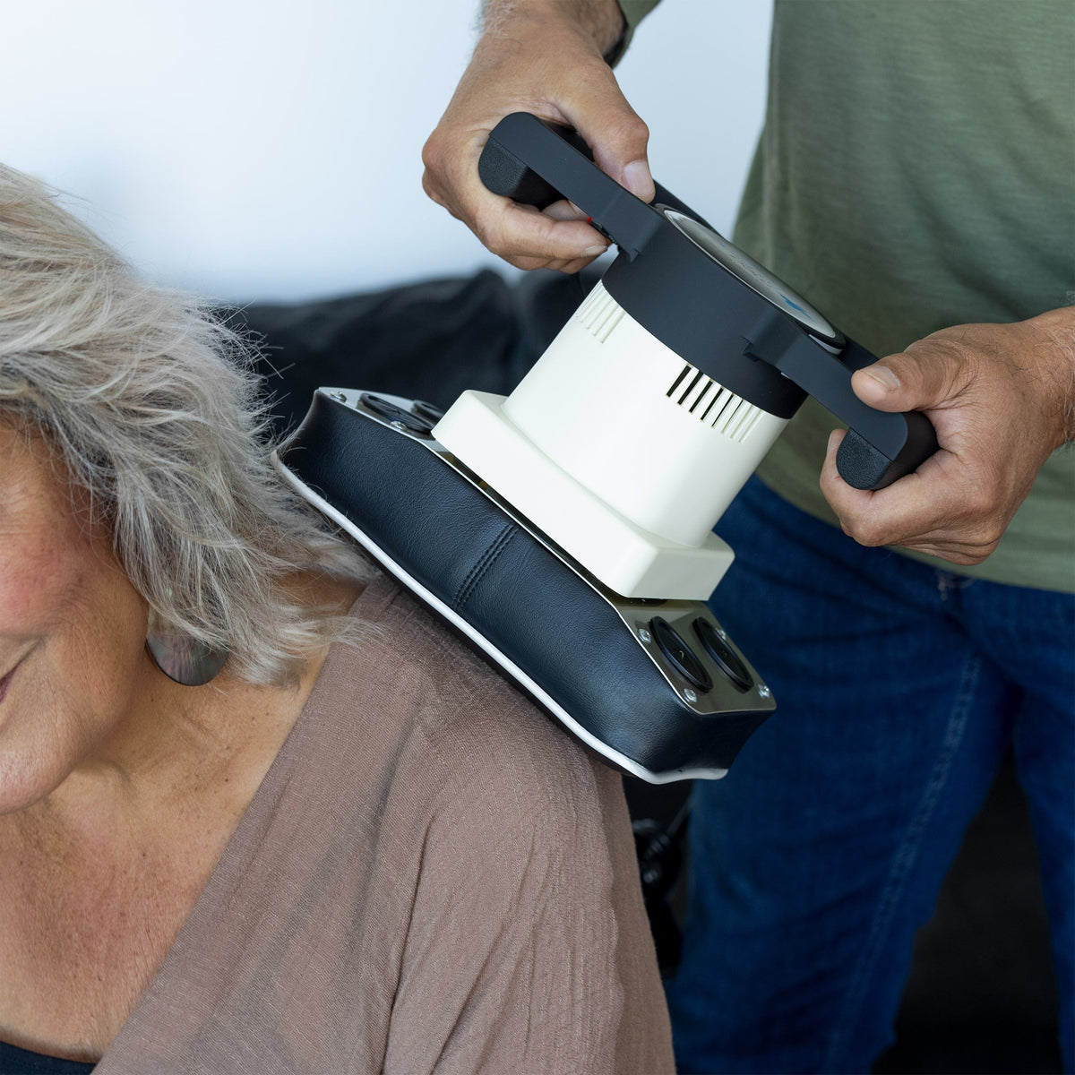 Body massager applied to a smiling woman’s shoulder as she sits, demonstrating use on upper body areas.