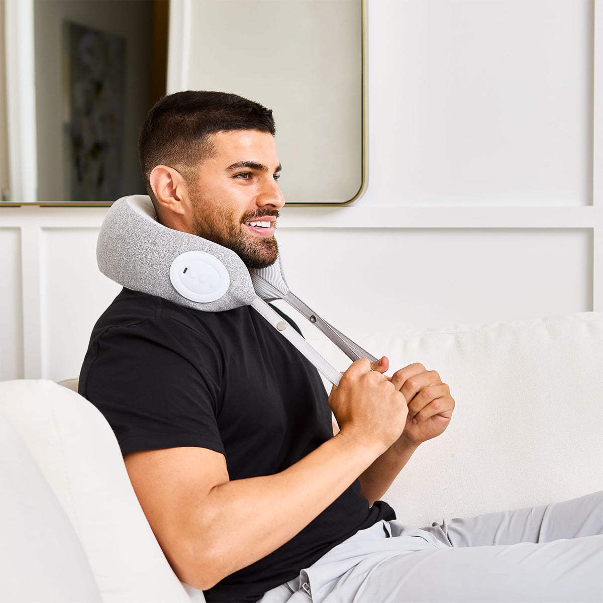 Man smiling on couch using MedMassager neck massager with hand straps for neck pain relief.