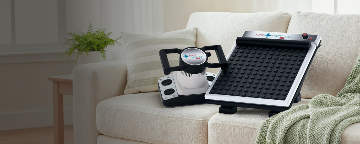 MedMassager foot massager and body massager on a beige sofa in a bright living room with a small plant on the side table.