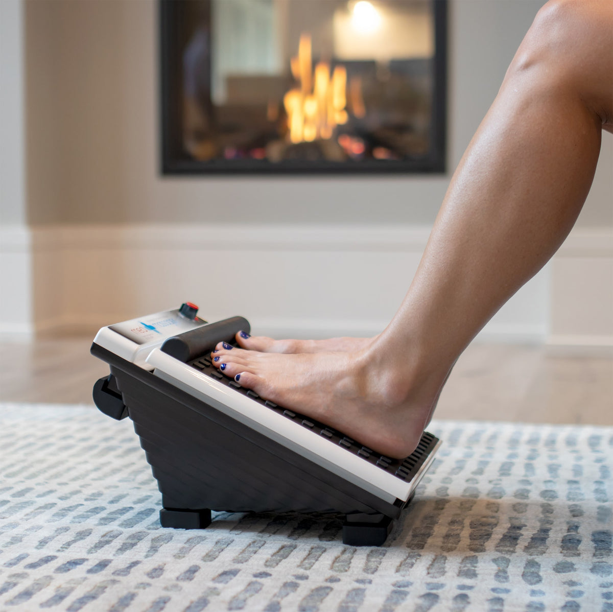 Foot massager in use on a rug in front of a fireplace, with one leg visible. Ideal for foot relaxation and comfort.